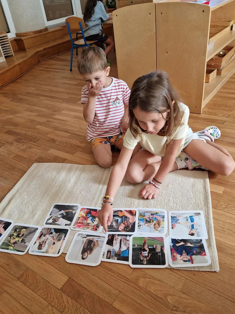 Doi copii de vârste diferite lucrând împreună cu cartonașe pe covoraș, la Arcadia Montessori