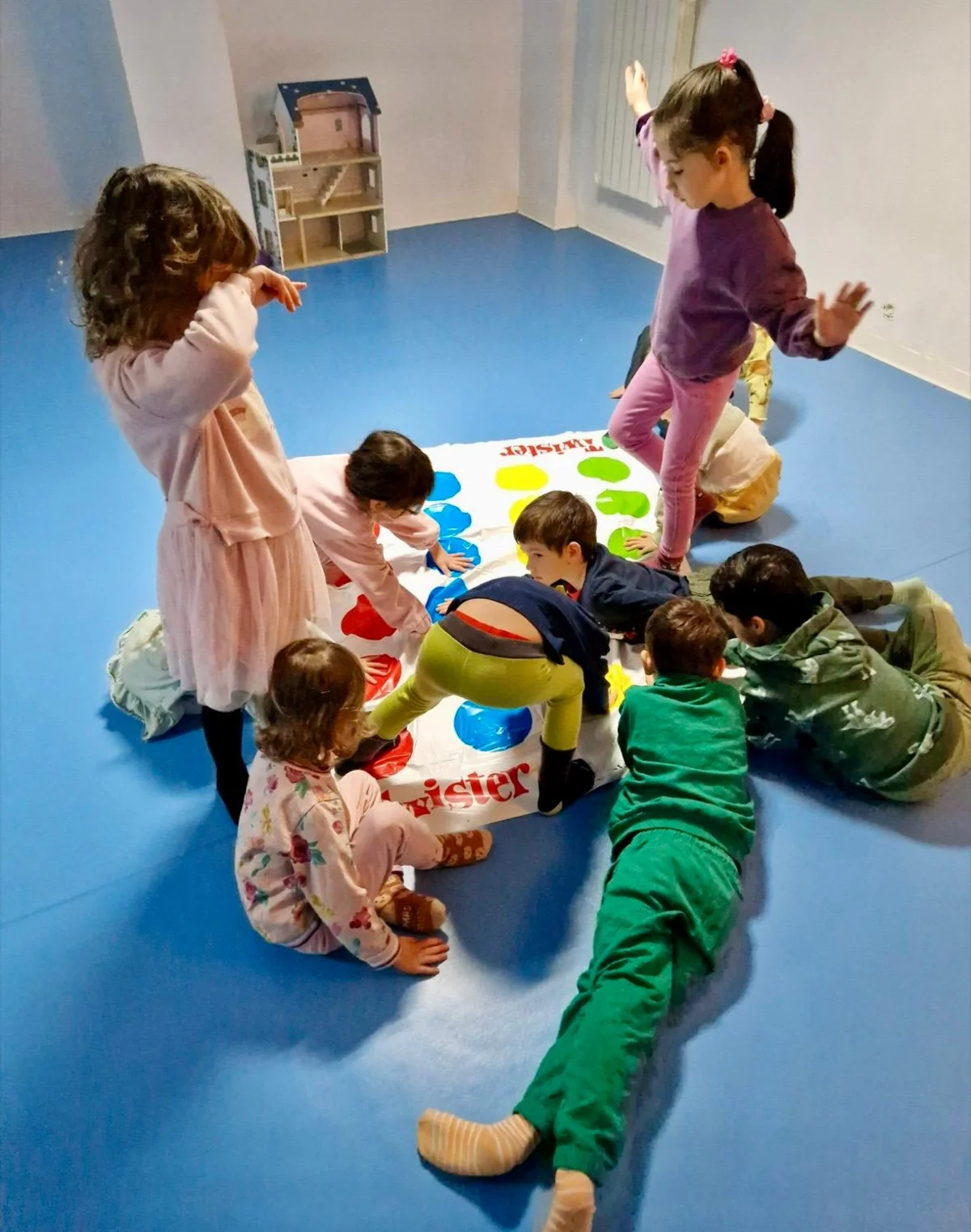 Copii jucând Twister pe covorul albastru din sala de sport Arcadia