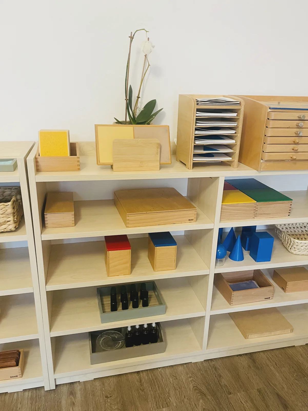 Rafturi cu materiale senzoriale Montessori, ordonate la înălțimea copiilor