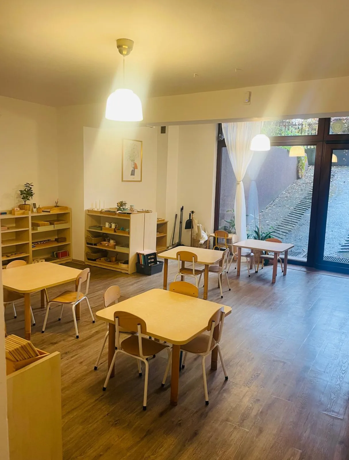 Clasă Montessori cu mese pentru copii și ușă spre grădină, Arcadia Montessori