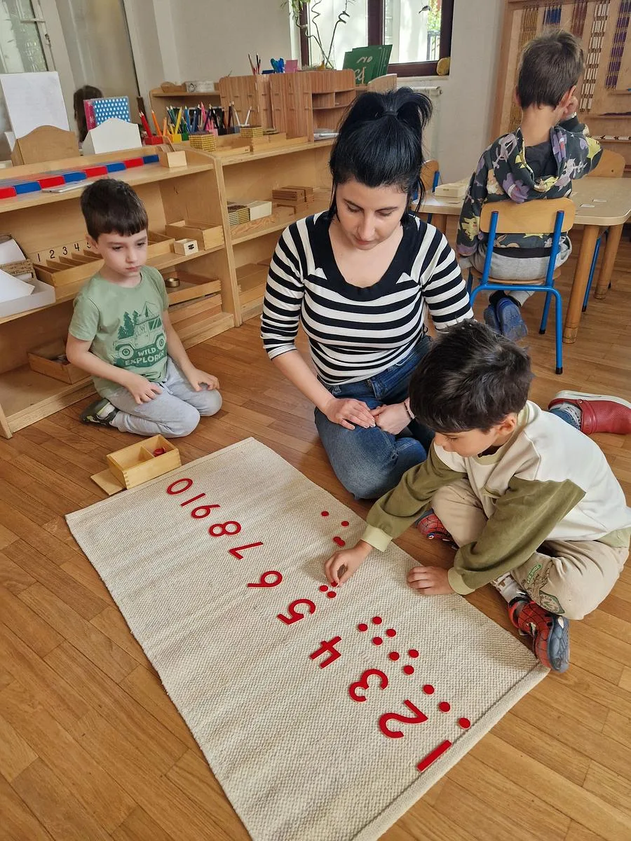 Educatoare lângă copii care lucrează cu cifrele și jetoanele Montessori, în Grupa 3-6 ani de la Arcadia Montessori din Corbeanca
